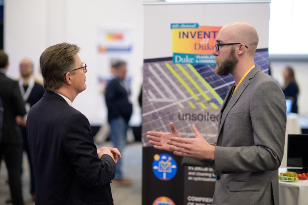 Michael Valerino, right, explains the problem of dirty solar panels to Duke University President Price.