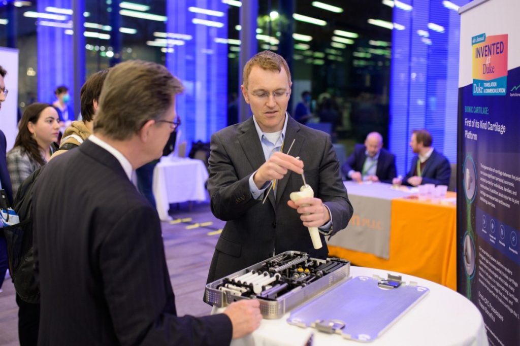 Benjamin Wiley, center, demonstrates Sparta Biomedical's implant technology to Duke University President Price and other attendees.