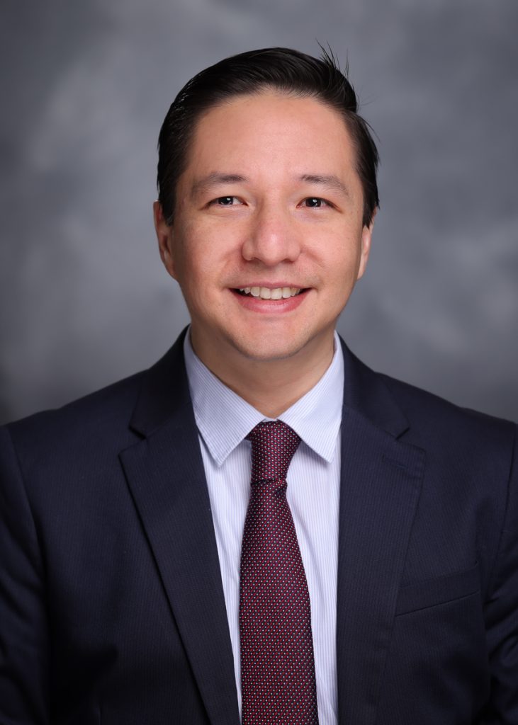 Headshot of David Chang Villacreses smiling directly at the camera, wearing a black suit jacket, white shirt, and dark red tie.
