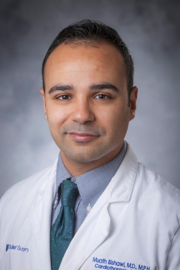 Headshot of Muath Bishawi, smiling slightly at the camera, in official white coat with Duke Surgery logo and his name spelled out over a blue dress shirt and green tie.