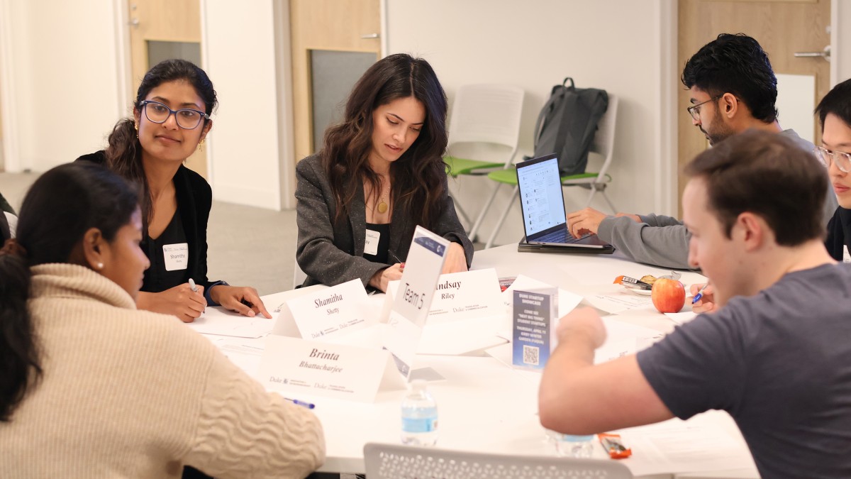 A team of professional students, including Shetty, converses and takes notes around a triangular table.