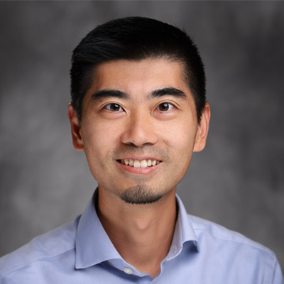 Headshot of Daniel Luo in a light blue dress shirt, on a mottled grey background. 